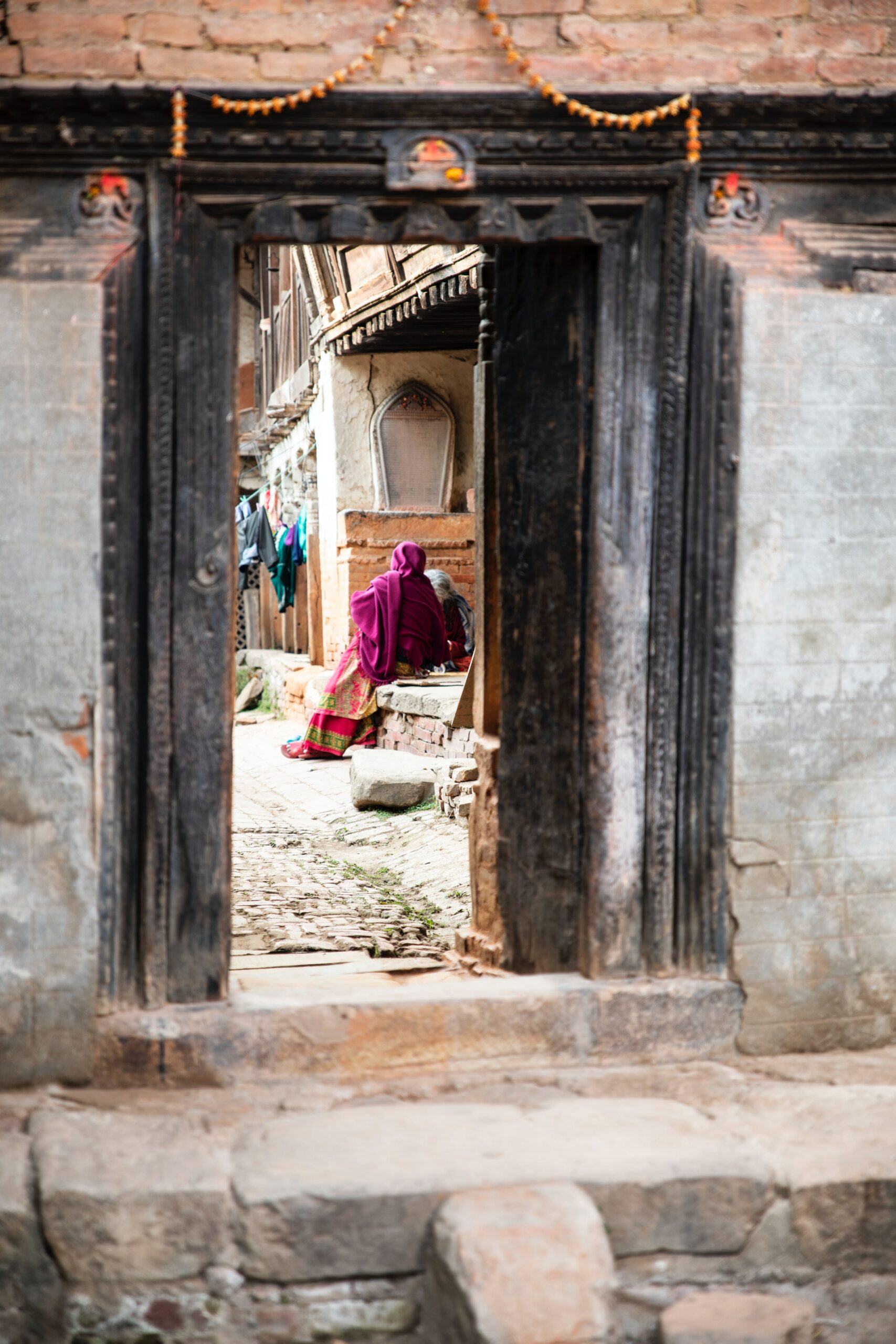 Two women sit conversing in the morning sun in Bhaktapur, Nepal.